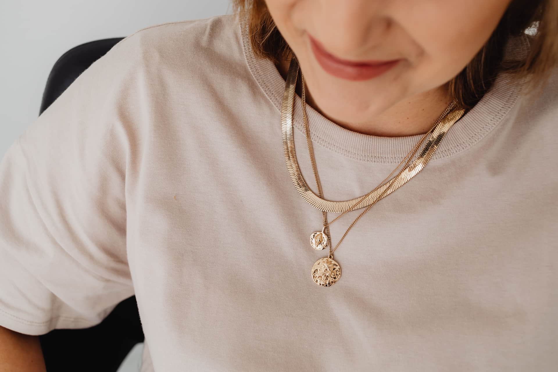 Layered gold-toned necklaces photographed on a neutral background
